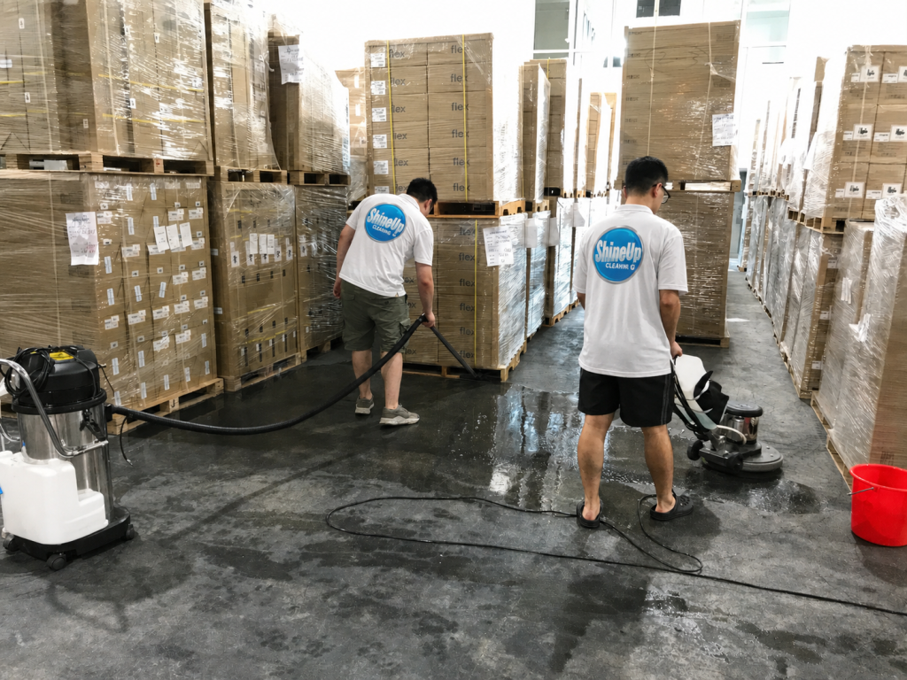 Two Shine Up Cleaning professionals performing warehouse floor cleaning in Chicago with industrial equipment and stacked pallets